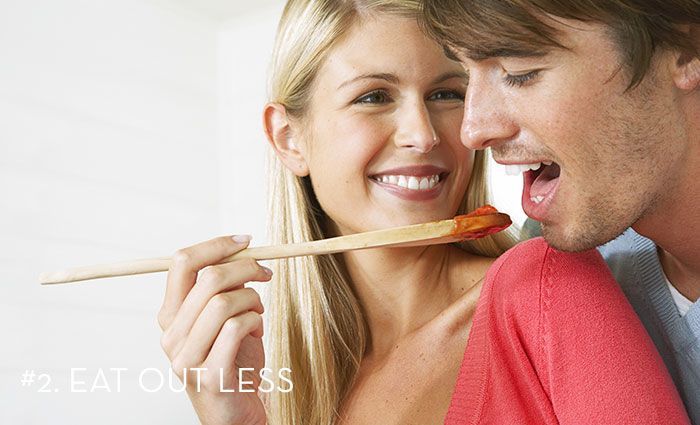 a woman feeding a man pasta sauce from a wooden spoon with the words Eat Out Less