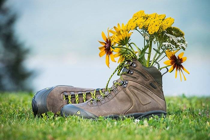 pair of hiking boots in front of lake with flower in them
